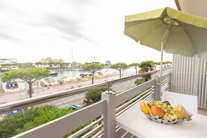 A balcony with a table holding a fruit basket, overlooking a marina with boats and trees. - Yachting Residence (Lignano Sabbiadoro)
