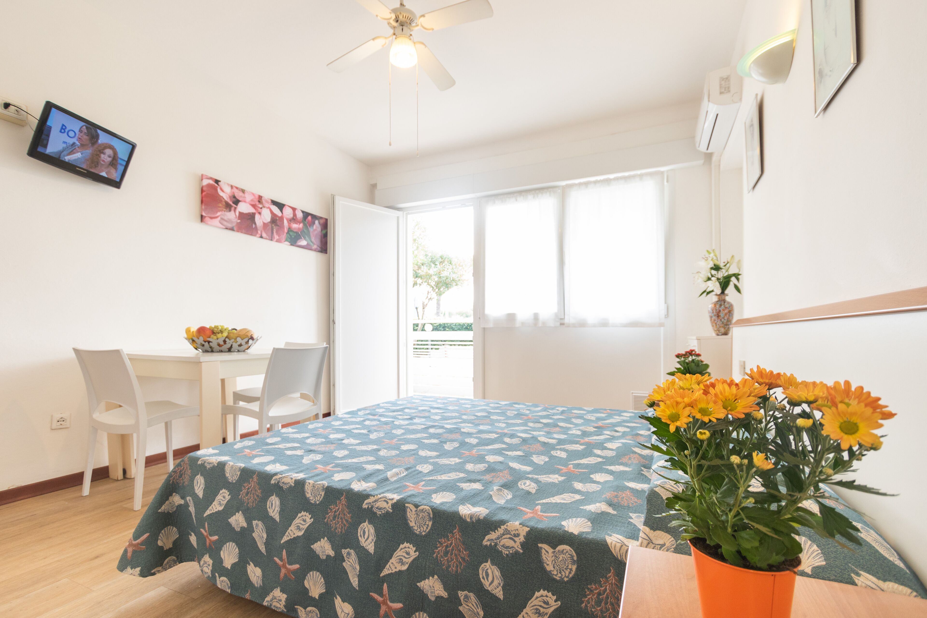 A bedroom with a bed, a desk, chairs, a TV, and a window.