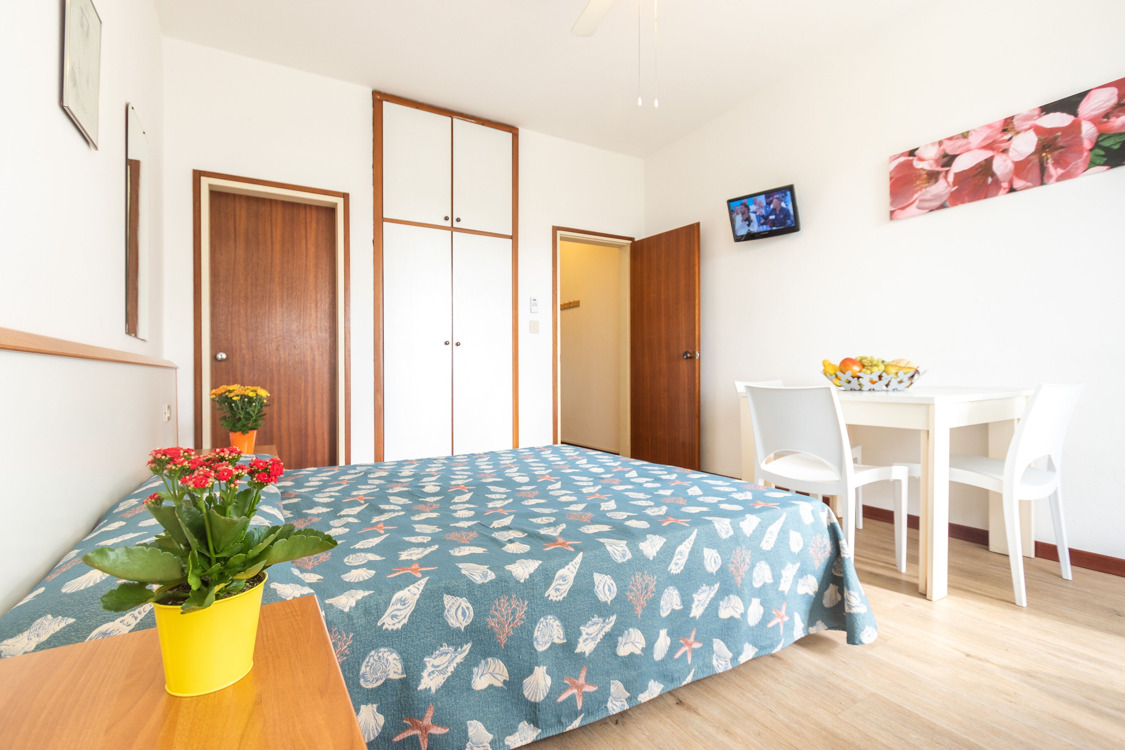 A bedroom with a bed, a desk, a chair, and a potted plant.