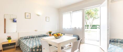 A bright room with a white ceiling fan, a dining table with chairs, a sofa, and a window with a view of greenery outside.