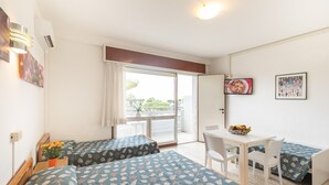 A hotel room with two beds, a dining table with chairs, and a view of the outdoors. - Yachting Residence (Lignano Sabbiadoro)