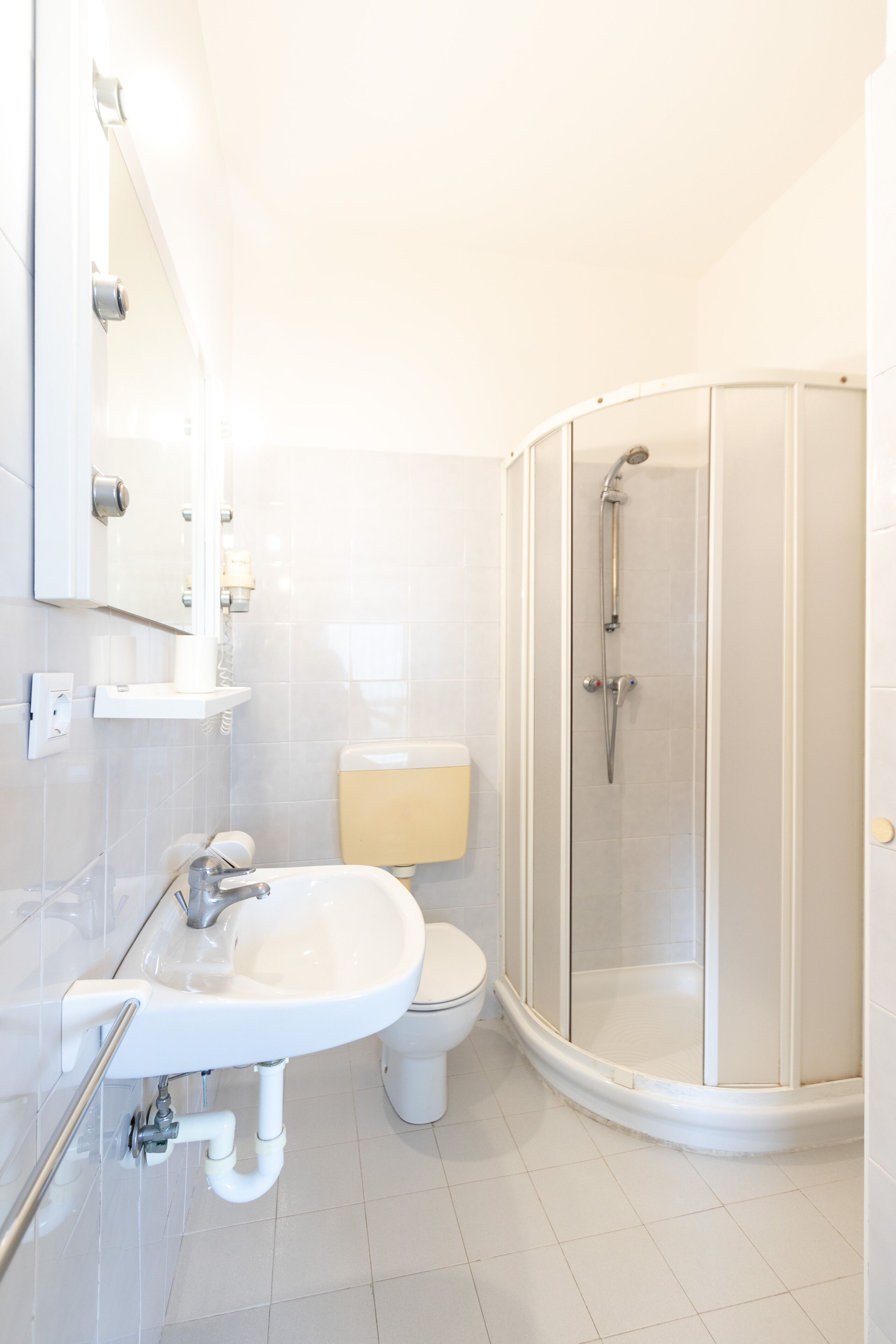 Un baño moderno con lavamanos blanco, inodoro y ducha con mampara de vidrio.
