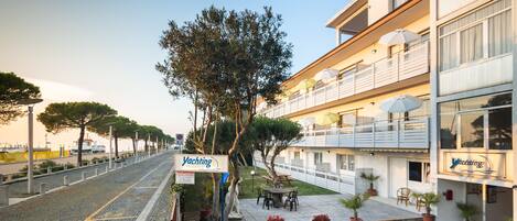 A waterfront hotel with outdoor seating, a sign for 'Yachting', and a view of the water.