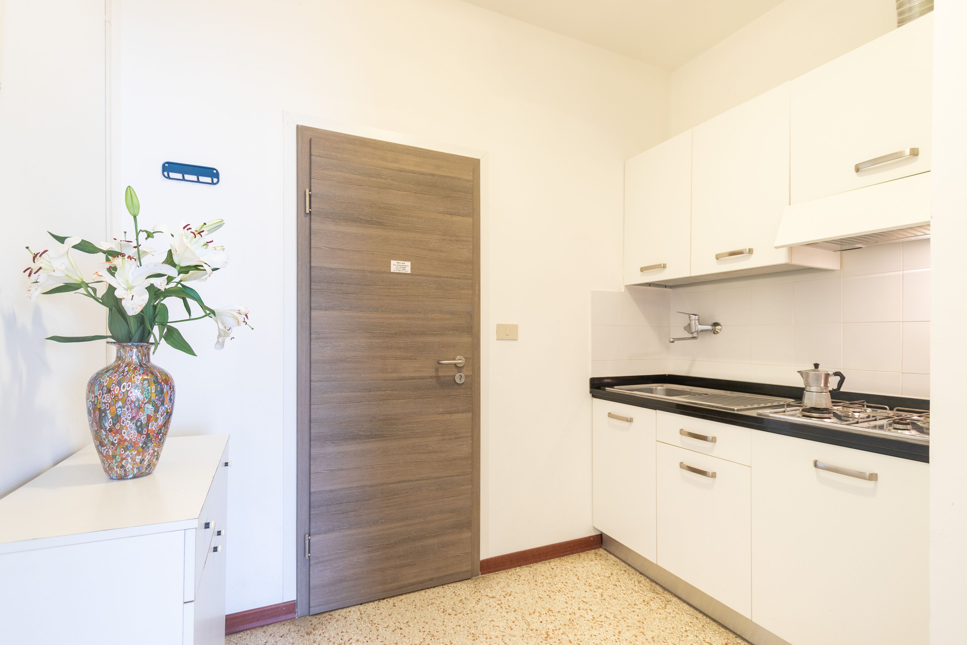 A kitchen with white cabinets, a wooden door, and a countertop with a coffee pot.