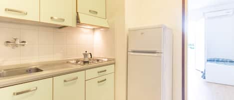 Una cocina con armarios de colores claros, un lavamanos de acero inoxidable y un refrigerador blanco.