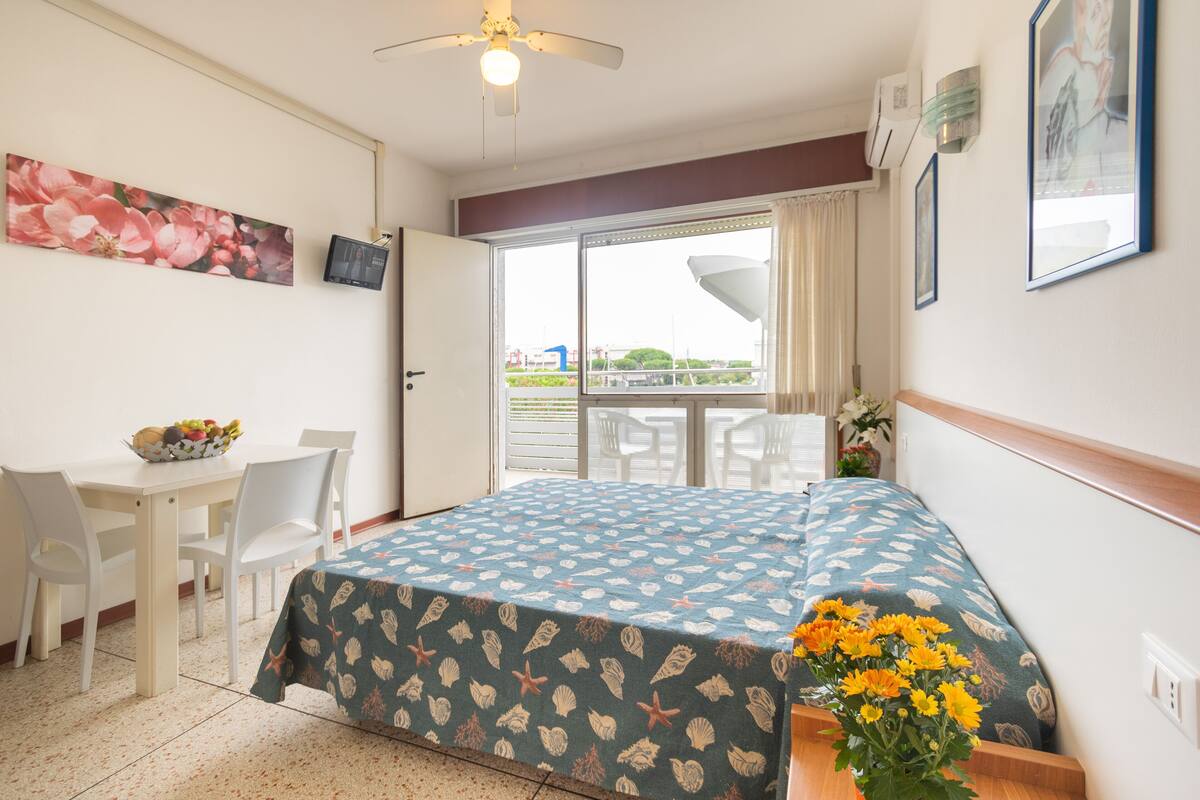 Een hotelkamer met een bed, een eettafel met stoelen, een televisie en een balkon met uitzicht.