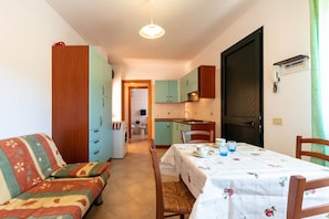 Un espacio habitable compacto con sofá, mesa de comedor, zona de cocina y lavadora.