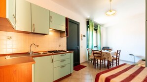 Une cuisine compacte équipée d’une cuisinière, d’un évier et de meubles de rangement verts. On y trouve également un coin repas avec une table et des chaises.