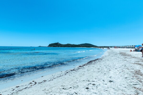 Una playa con aguas azules cristalinas, una orilla arenosa y una colina distante.