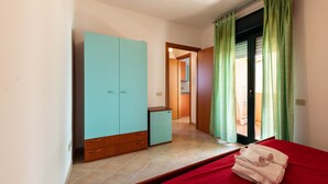 Une chambre à coucher comprenant un lit, une armoire, un petit meuble et une porte donnant sur un balcon.