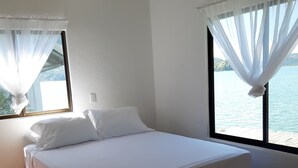 A bedroom with a bed, a window with sheer curtains, and a view of the water. - Vista Castillo Hotel (Golfito)