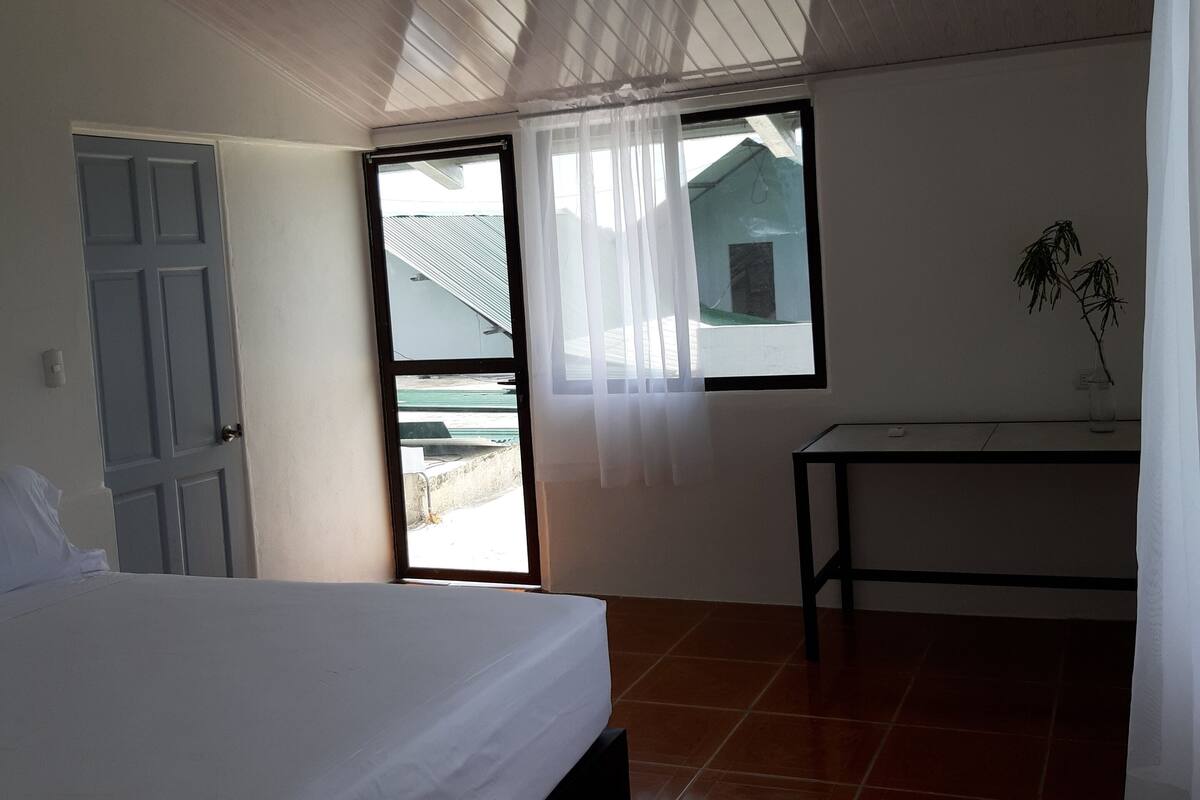 A bedroom with a bed, a window, a table, and a door.