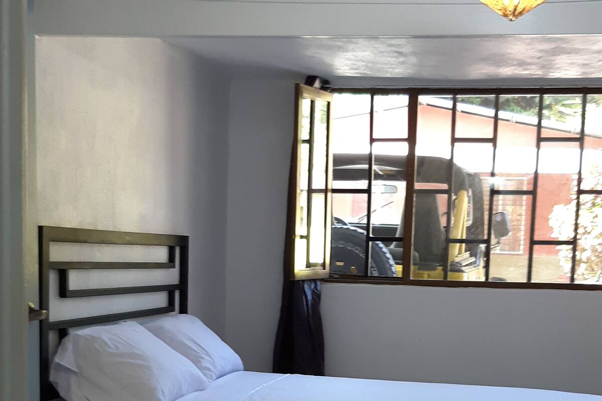 A single bed with a wooden headboard, a window with bars, and a tiled floor.