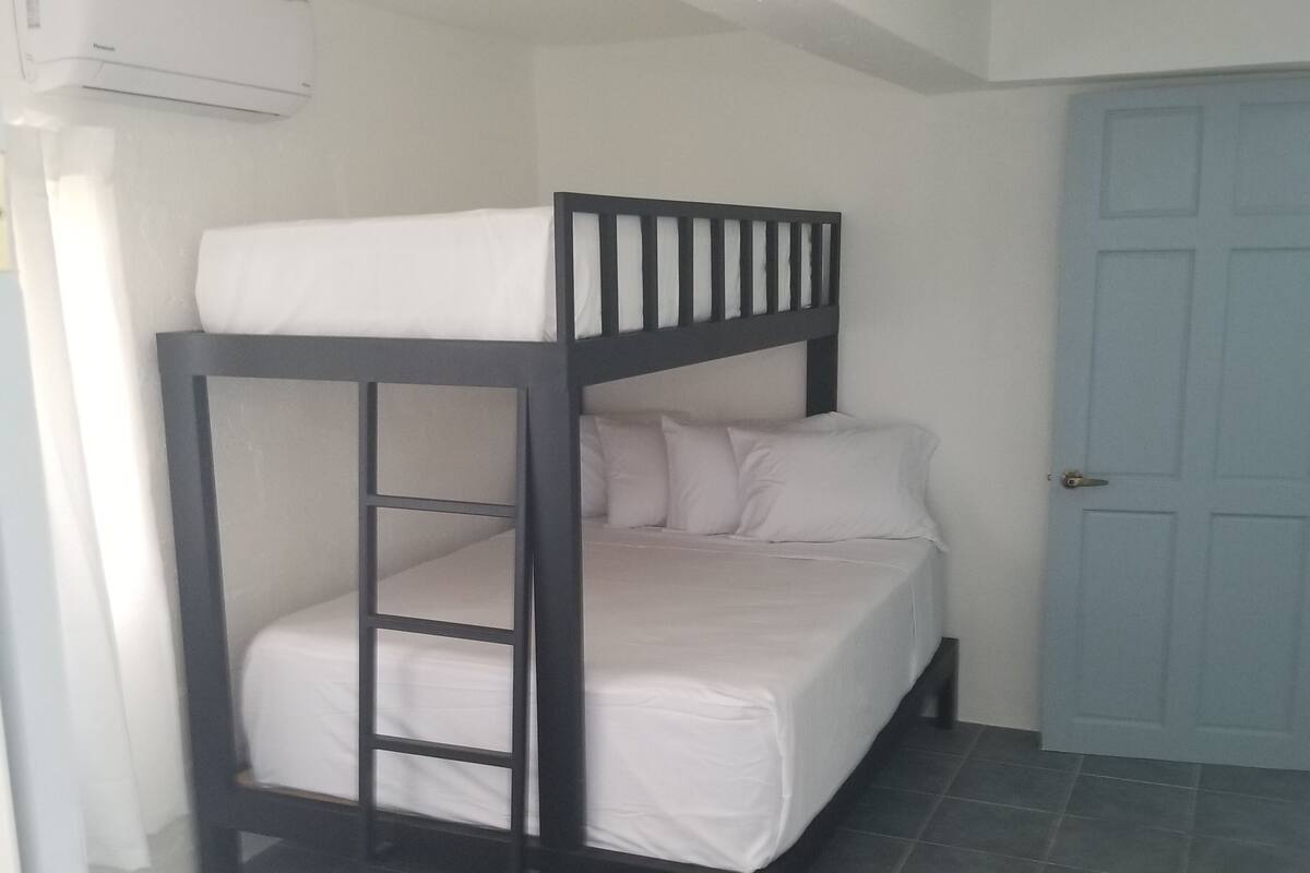 A bunk bed with a white mattress and pillows, a small shelf, and a door to the right.