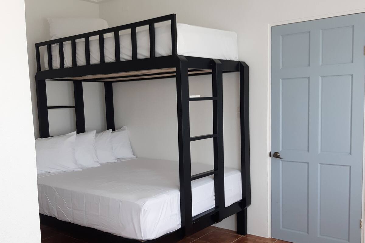 A bunk bed with white bedding in a room with brown tiled flooring and a blue door.