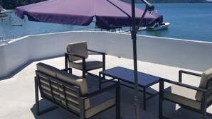 An outdoor seating area with a table and chairs, a purple umbrella, and a view of a lake with boats. - Vista Castillo Hotel (Golfito)