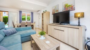 Una sala de estar moderna con un sofá, televisor, mueble de madera y una zona de comedor con mesa y sillas.