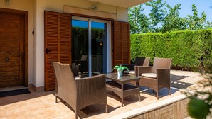 Un patio al aire libre con mobiliario de mimbre, una mesa de vidrio y una planta en maceta.