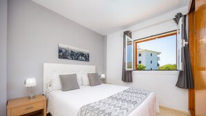Un dormitorio con cama, mesita de noche, lámpara y una ventana con cortinas.