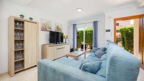Una sala de estar moderna con sofá, televisor, mueble de madera y vistas al verdor exterior.