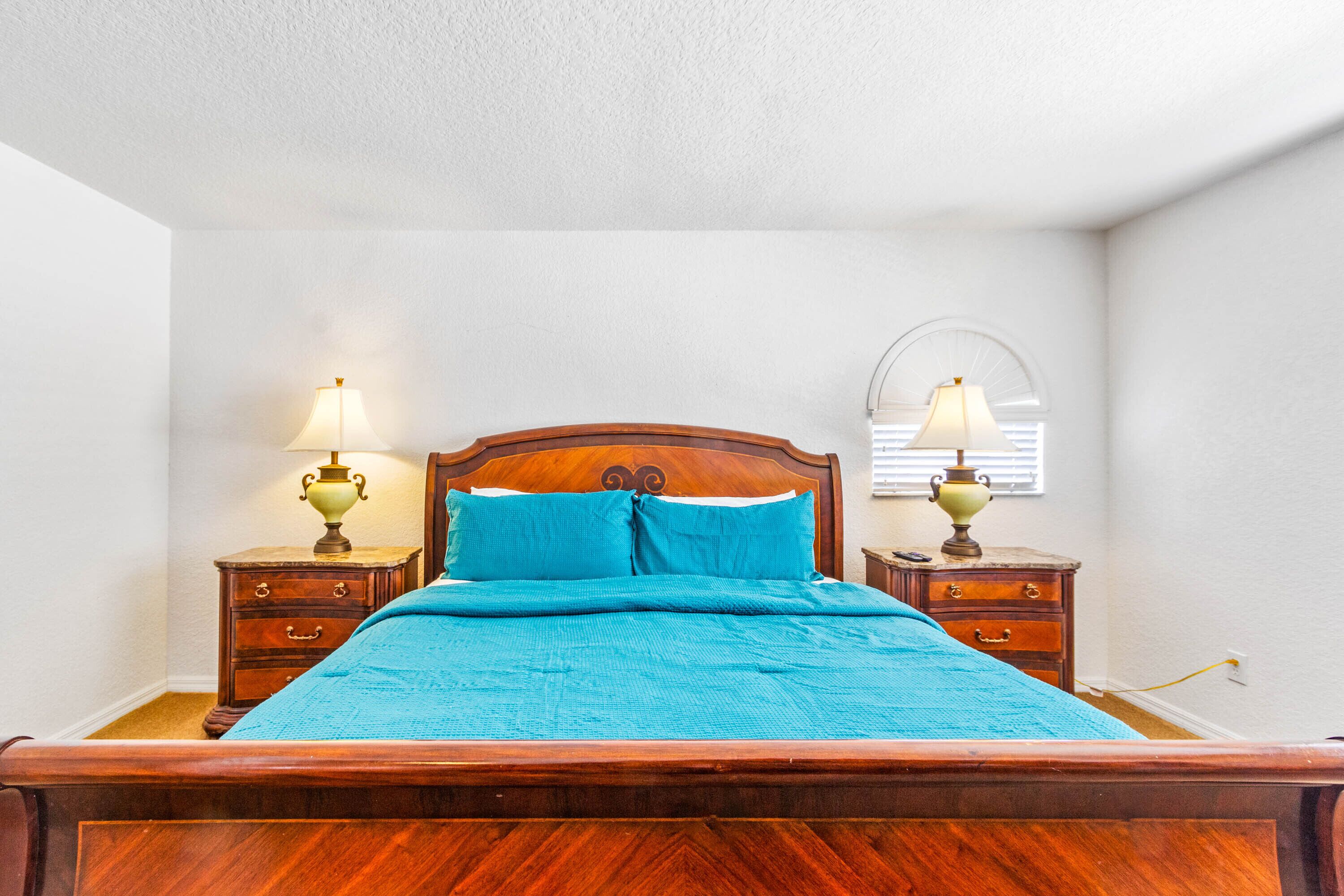 A bedroom with a wooden bed, two bedside tables with lamps, and a window with blinds.