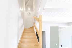 A wooden staircase with a handrail, leading to a room with a white wall and a light switch.