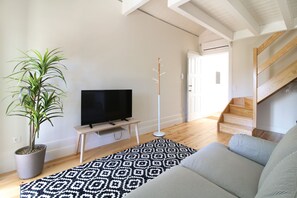 A modern living room with a flat-screen TV, a potted plant, a patterned rug, and a staircase with wooden steps.