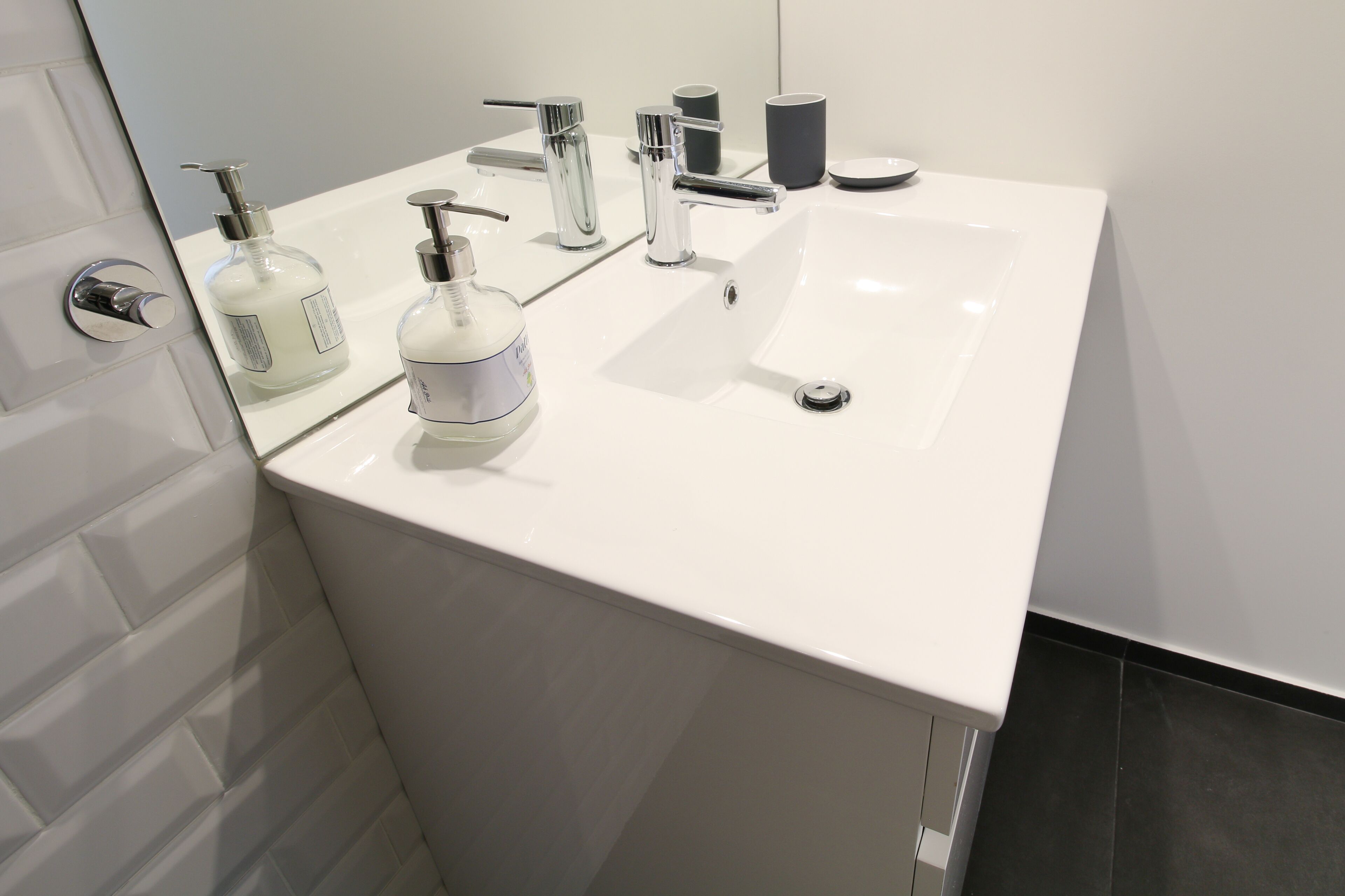 A modern bathroom with a white sink, chrome faucet, and two bottles of liquid soap.