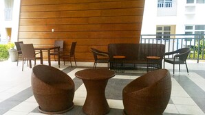 Een overdekt terras met rieten meubels, zoals stoelen en een bank, tegen een houten wand.