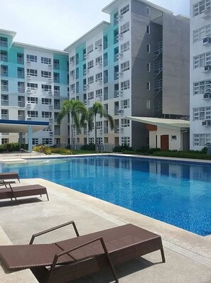 Une piscine entourée de chaises longues, elle-même bordée d’immeubles résidentiels à plusieurs étages dotés de balcons.