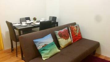 A living area with a brown sofa, two pillows, a dining table with chairs, and a small plant.