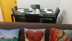 Een eetgedeelte met een tafel gedekt voor vier personen, een kleine bloempot en een hartvormig kussen op de bank.