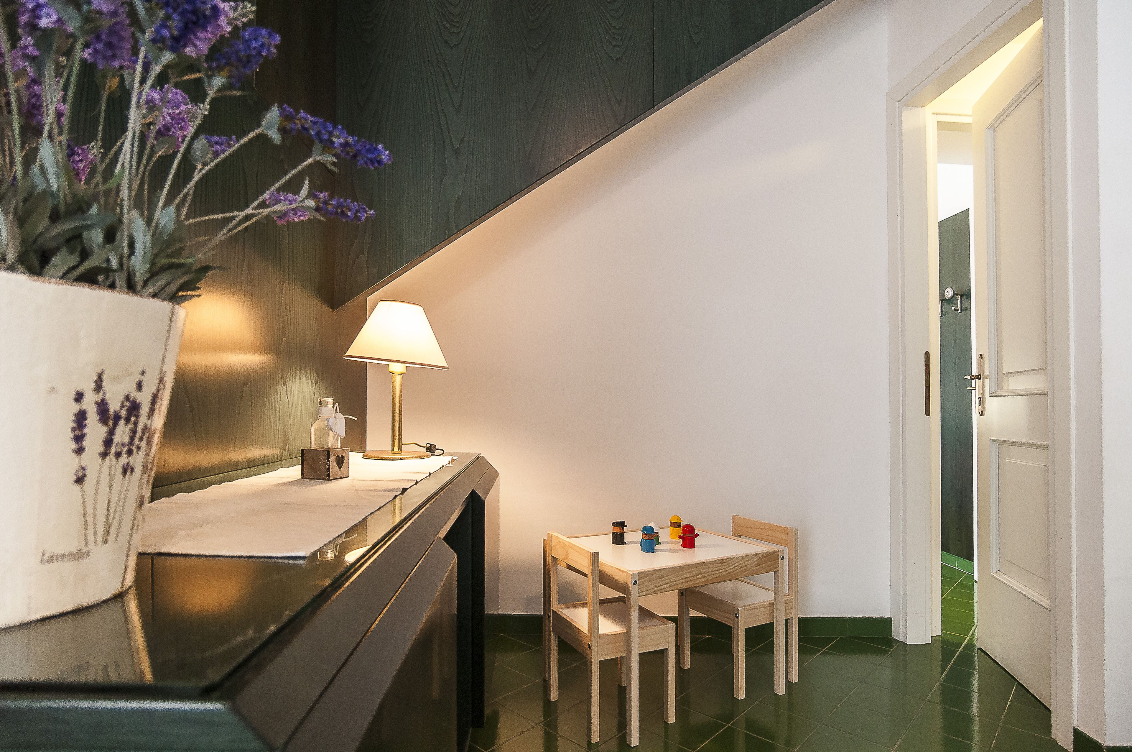 Een gezellig eethoekje met een tafel, stoelen, een lamp en een bloemetjesvaas.