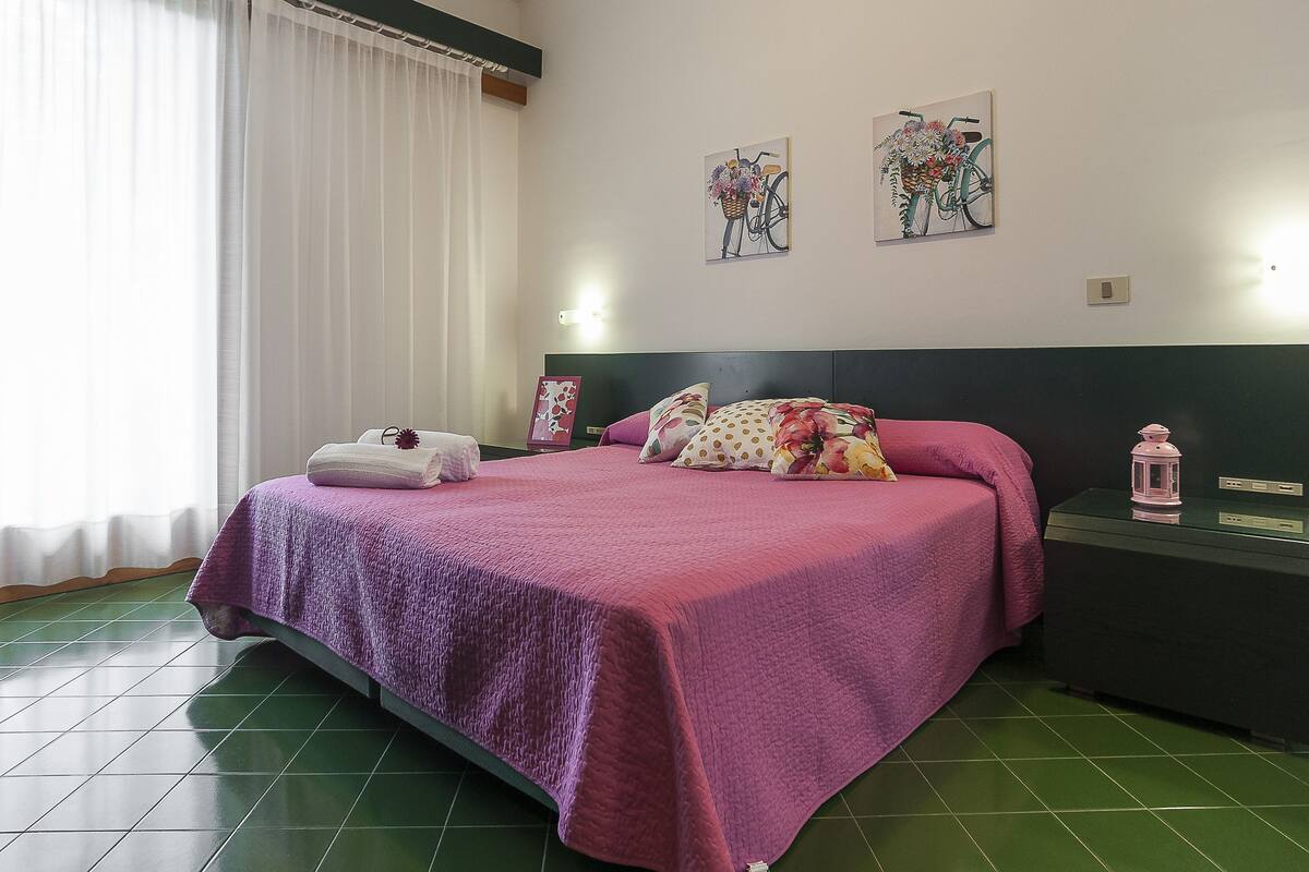 A room with a bed, a nightstand, a lamp, and artwork on the wall.