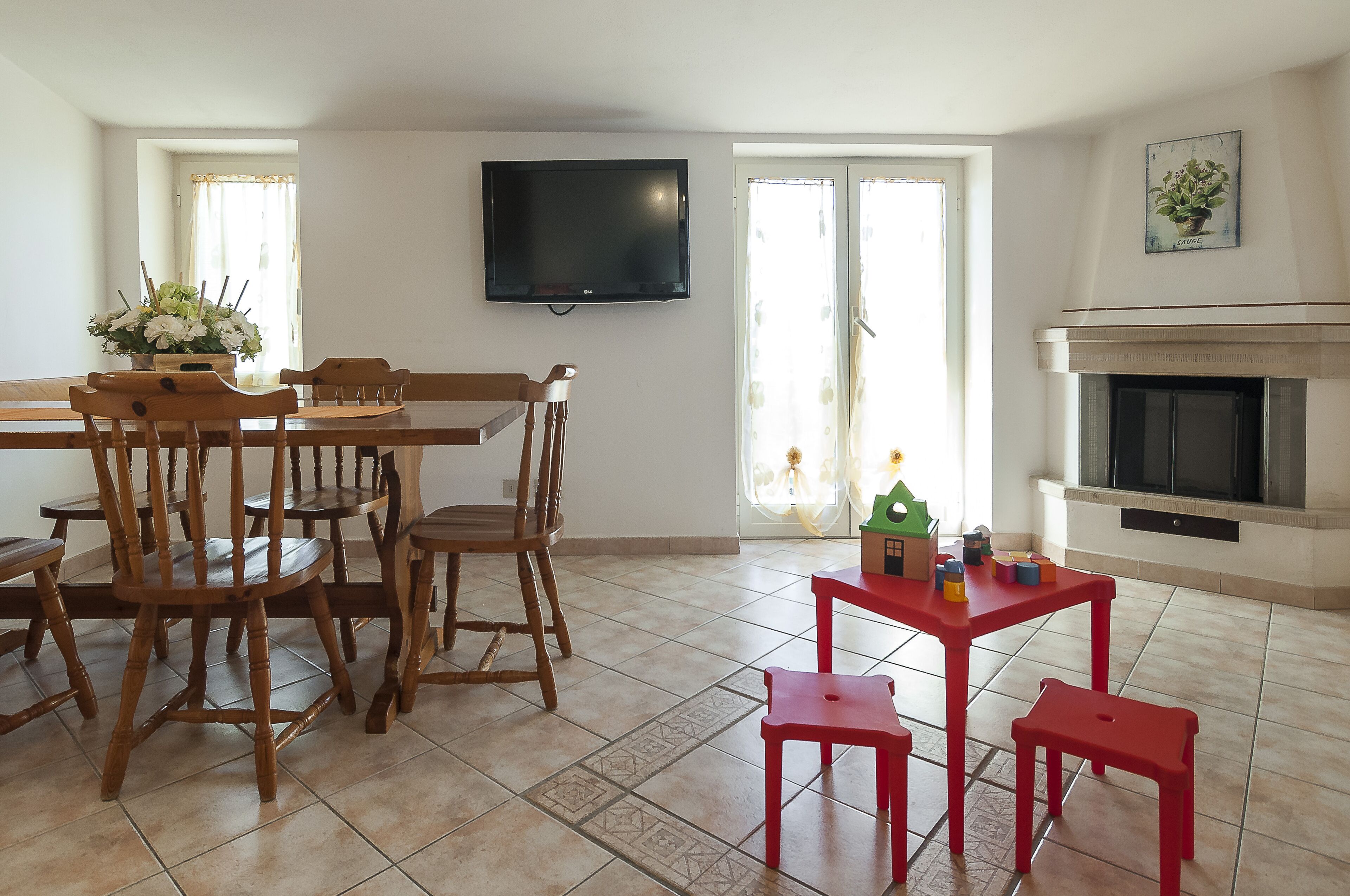 A dining area with wooden chairs and a table, a television mounted on the wall, and a fireplace.