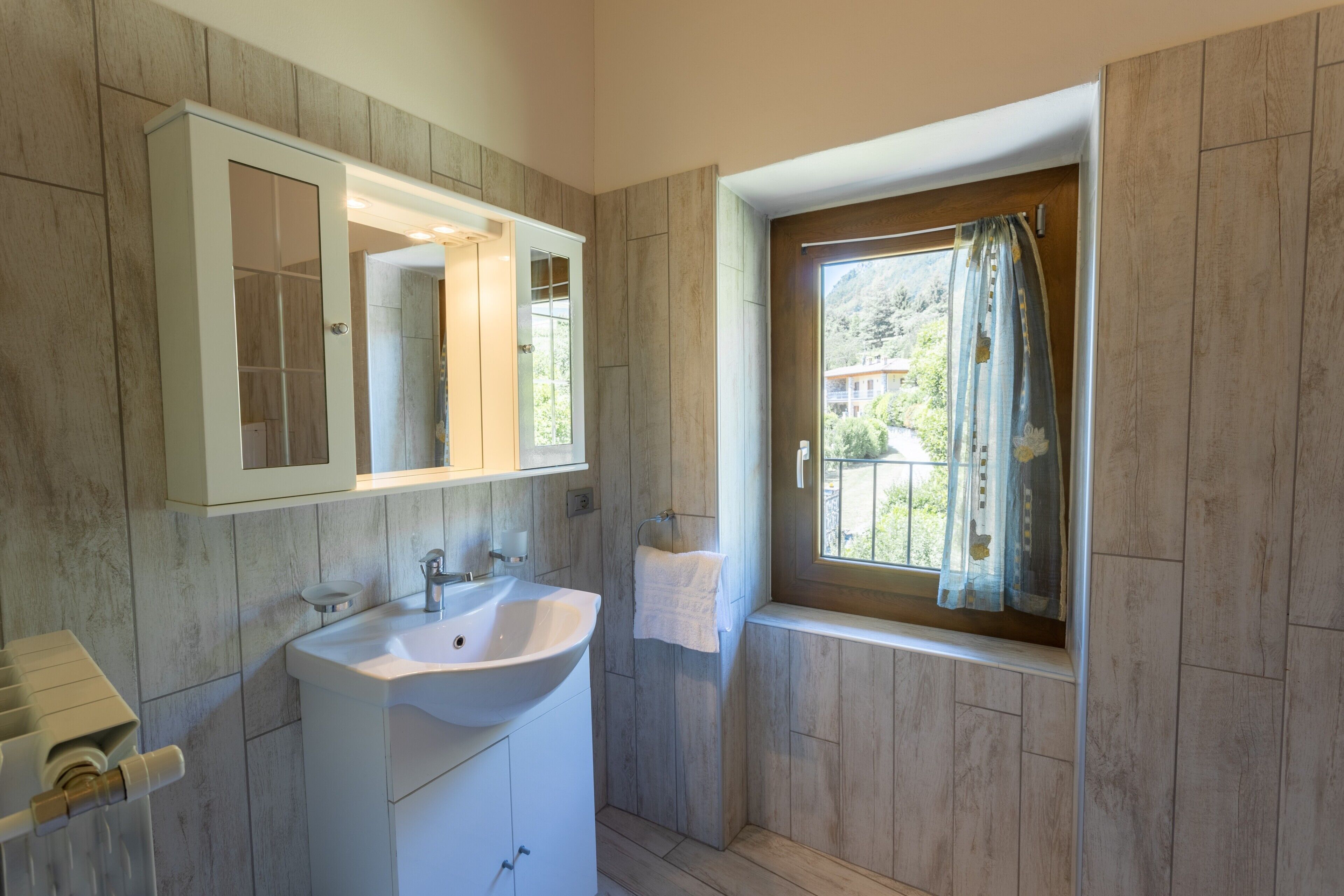 Un bagno con lavandino, specchio e finestra con tende.