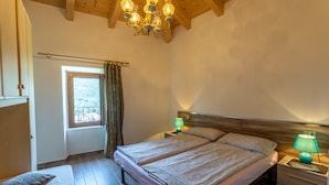 Ein Schlafzimmer mit Holzboden, einem Bett mit gemusterten Betttextilien, Nachttischlampen und einem Fenster mit Vorhängen.