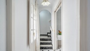 A hallway with white walls, a black and white tiled floor, a staircase, and a chandelier.