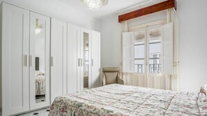 A bedroom with a bed, a wardrobe, a chair, and a window with curtains.
