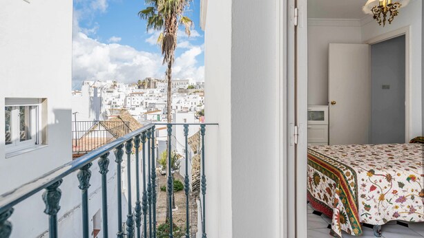 A balcony with a view of a white building complex, a palm tree, and a bed with a floral bedspread.