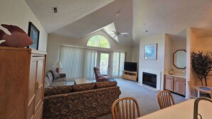 A spacious living room with a high ceiling, a fireplace, a television, and a dining area with wooden furniture. - Tidewater- Teal lake #2521 (North Myrtle Beach)