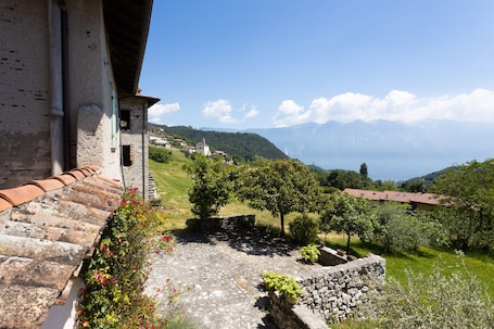 A stone building with a tiled roof, a stone wall, and a garden with trees and flowers.. Apartment 'Artù' with Shared Garden, Balcony and Wi-Fi