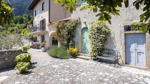 Un patio empedrado con un banco, plantas en macetas y un edificio con puerta verde y balcón.