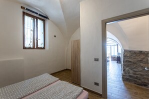 Une chambre à coucher avec un lit, une fenêtre avec des rideaux, une armoire et un mur en pierre.