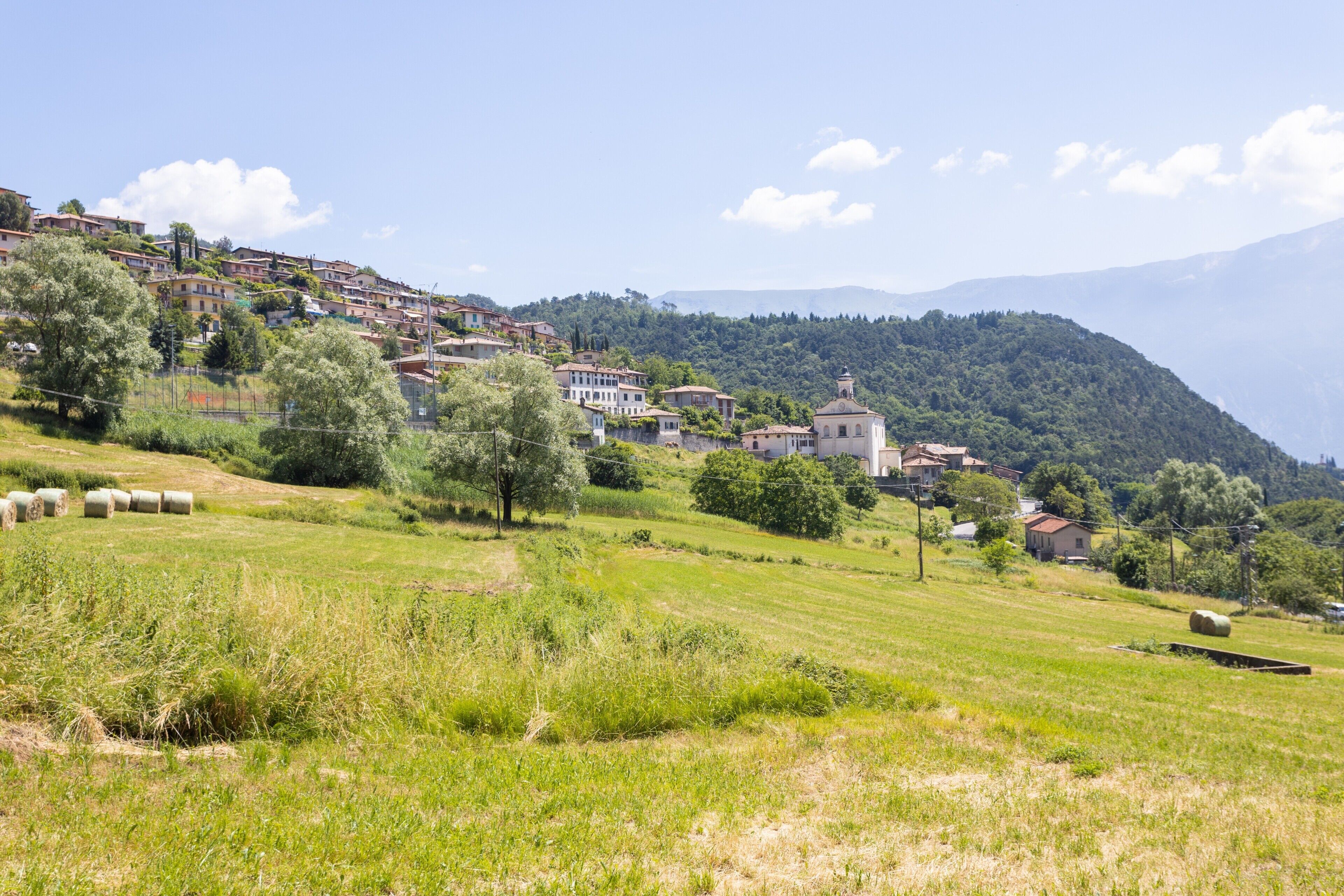 A hillside village with houses, a church, and hay bales in a green field.