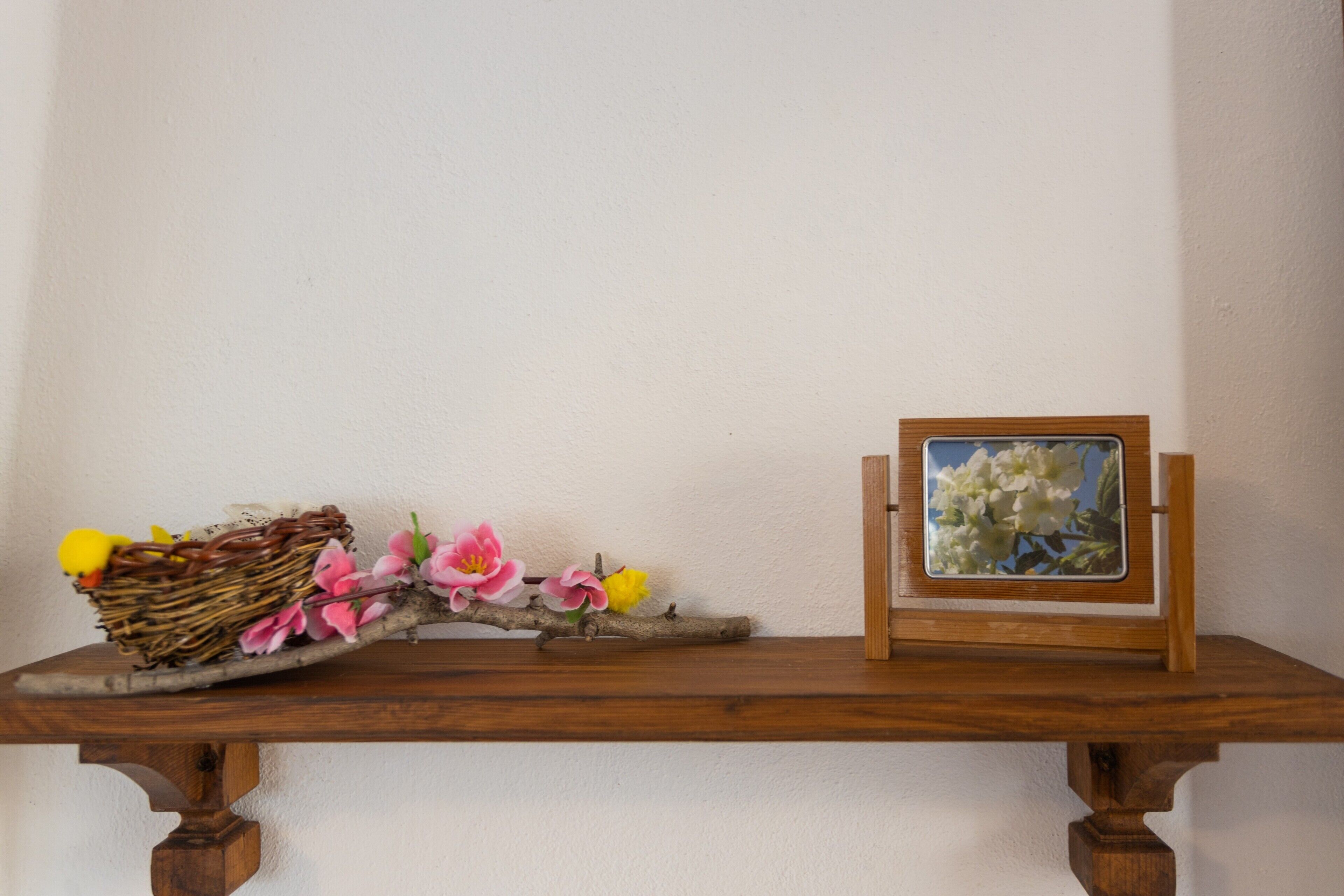 A wooden table with a wicker basket, pink flowers, and a framed picture.