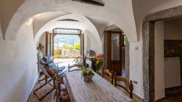 Une pièce comprenant une table à manger, des chaises, une vue sur l’extérieur par une arche et un mur en pierre.