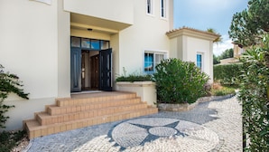 Una casa con entrada pavimentada, un diseño de mosaico circular y un jardín con diversas plantas.