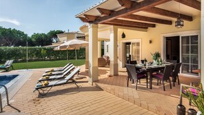 Un patio techado con piscina, sillas de descanso y comedor con mobiliario exterior.