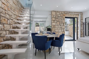 A modern interior with a stone wall, a staircase, a dining area with blue chairs, and a bed. - Dion Villa Zakynthos Greece One Bedroom Villa With Private Pool No01 (Zakynthos)